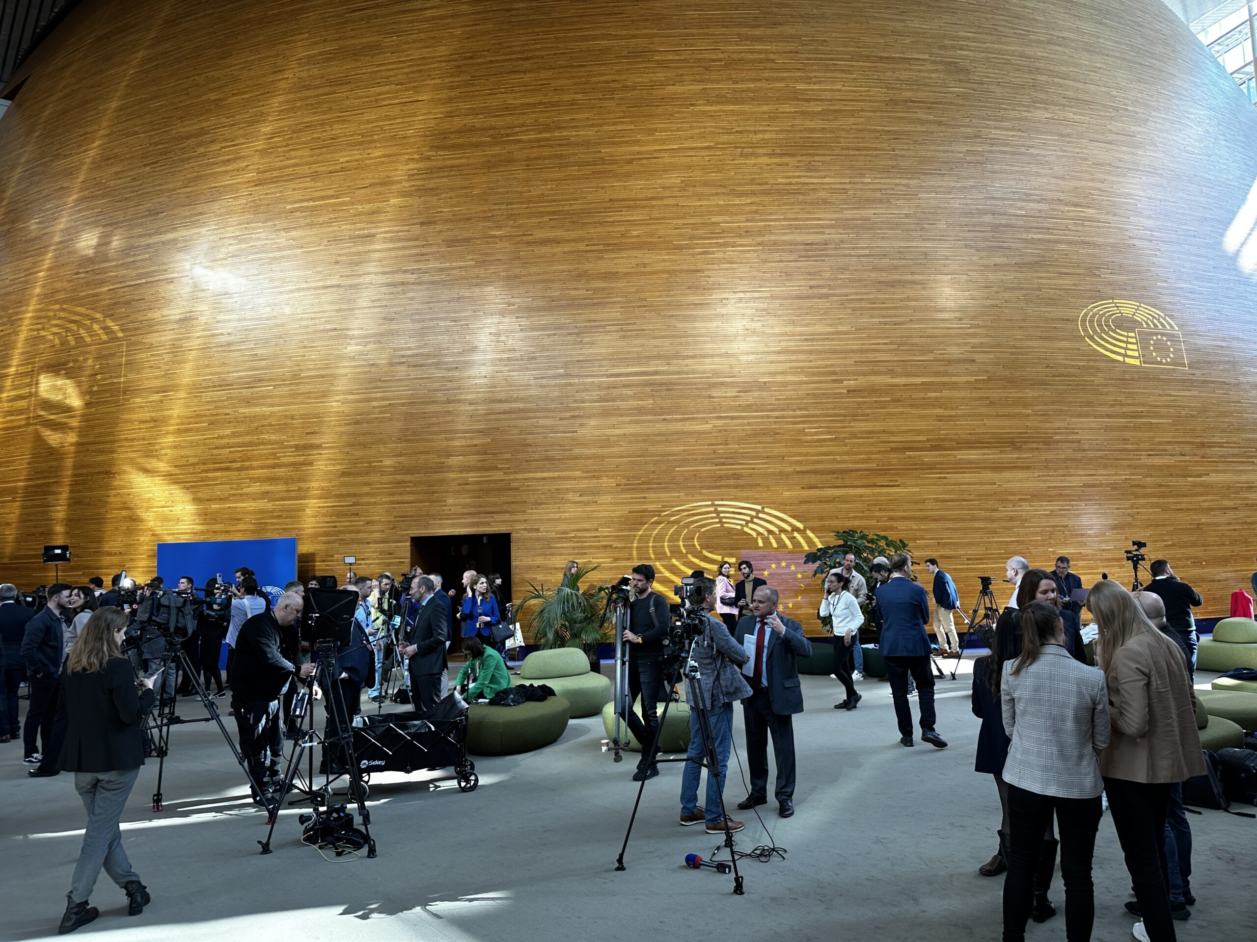 Journalists stand in front of cameras mounted on tripods, waiting for EU dignitaries to walk by. 