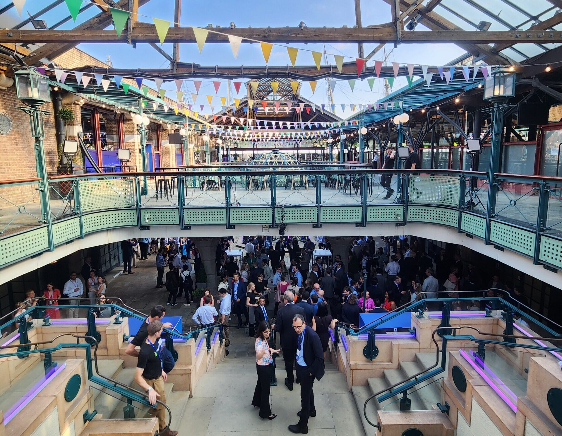 A large refurbished industrial space with steel beams and a glass ceiling. People mill about below.