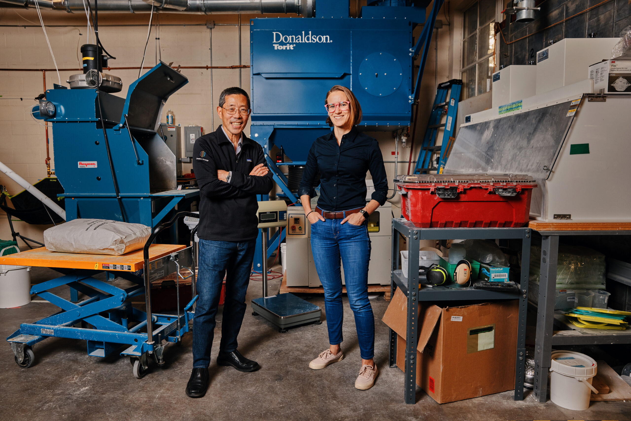 Two people (a man and a woman) pose with heavy duty lab equipment. Both are smiling.