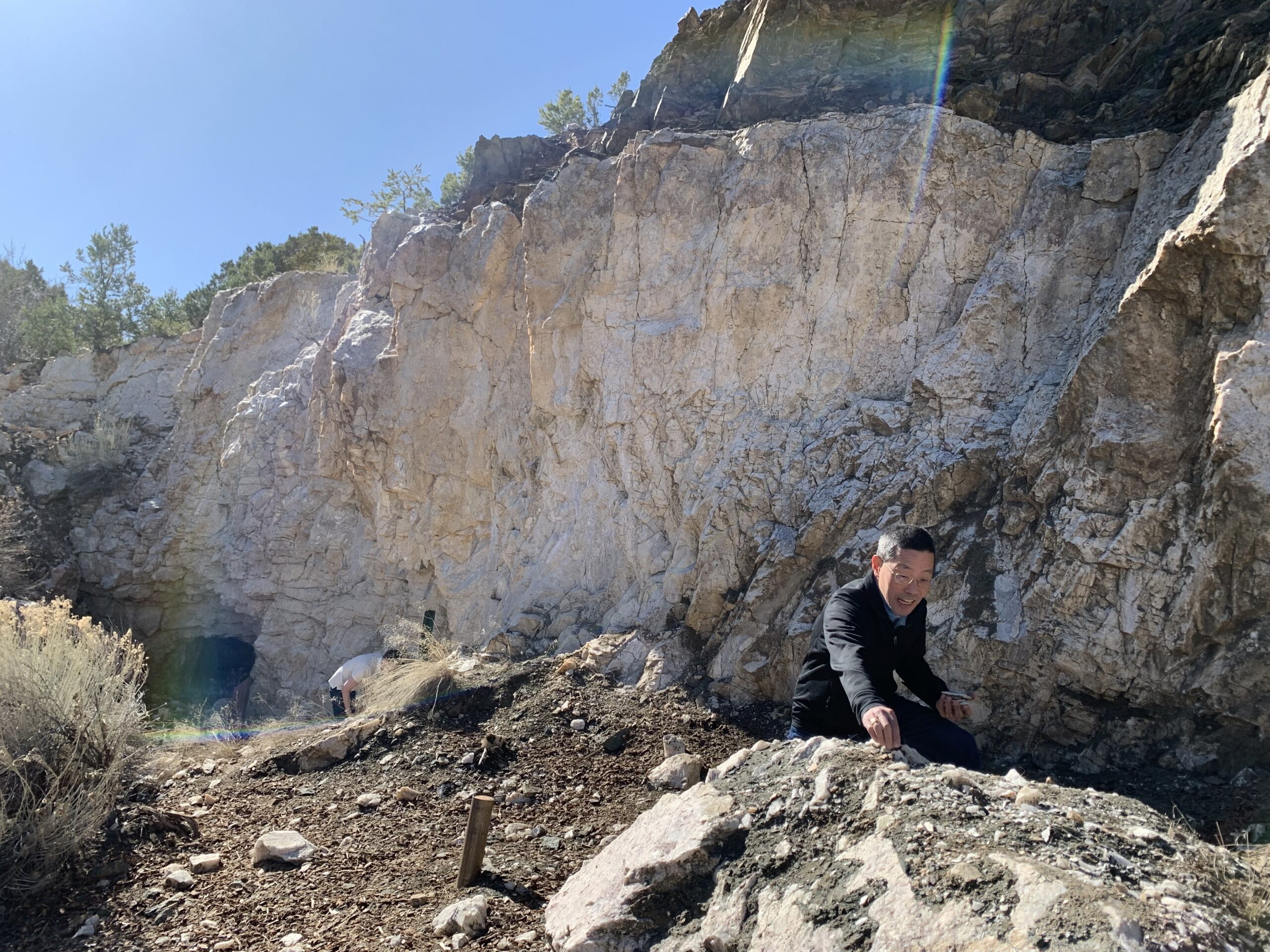 A man excitedly collects rock in front of a sheer rock face.