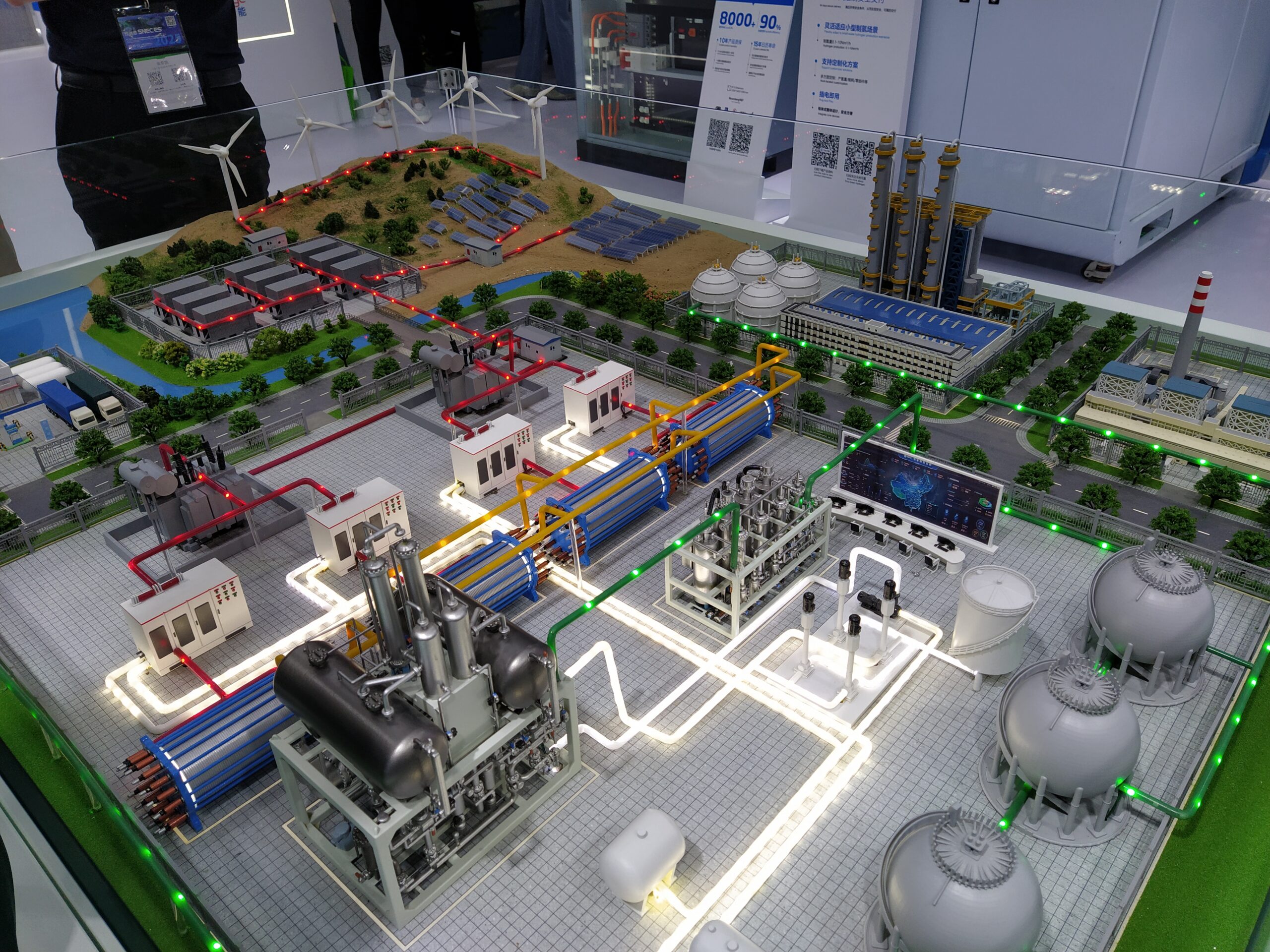 A miniature, tabletop model of a large renewable energy plant and factory is on display at a conference. The model includes light up red and green lights and looks convincingly life-like.