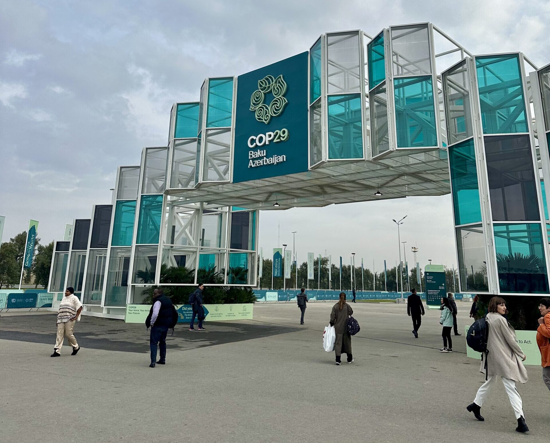 The official entrance of the COP29 summit featuring panels of blue and white glass and a sign in the middle that says "COP29."