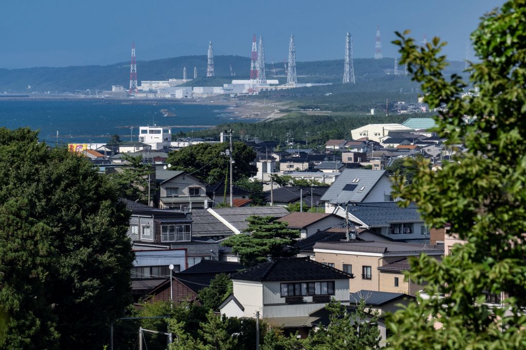 A photo of a large industrial plant (a nuclear power plant) in the distance next to a large body of water. In the foreground, there are houses clustered on a hill.