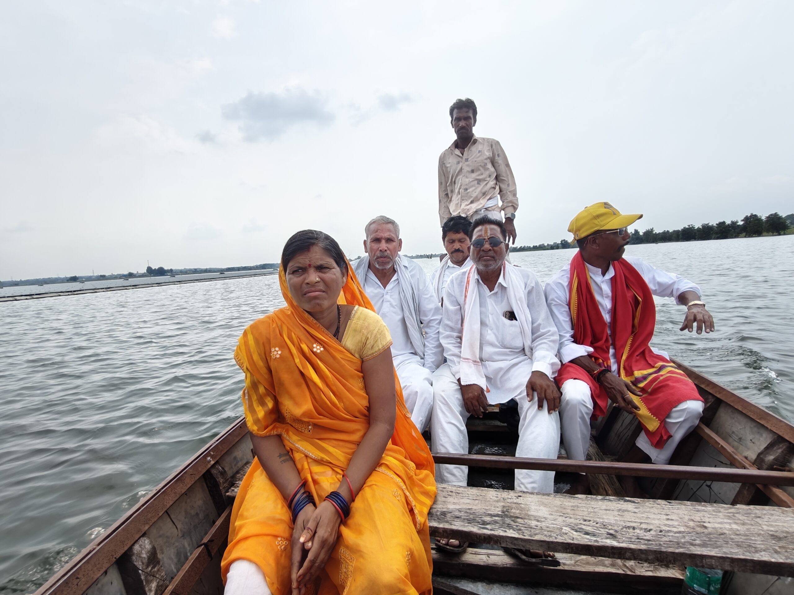 Photo of villagers from rural India in a wooden boat on a lake where solar panels have been installed on the water. Indian woman in an orange sari.