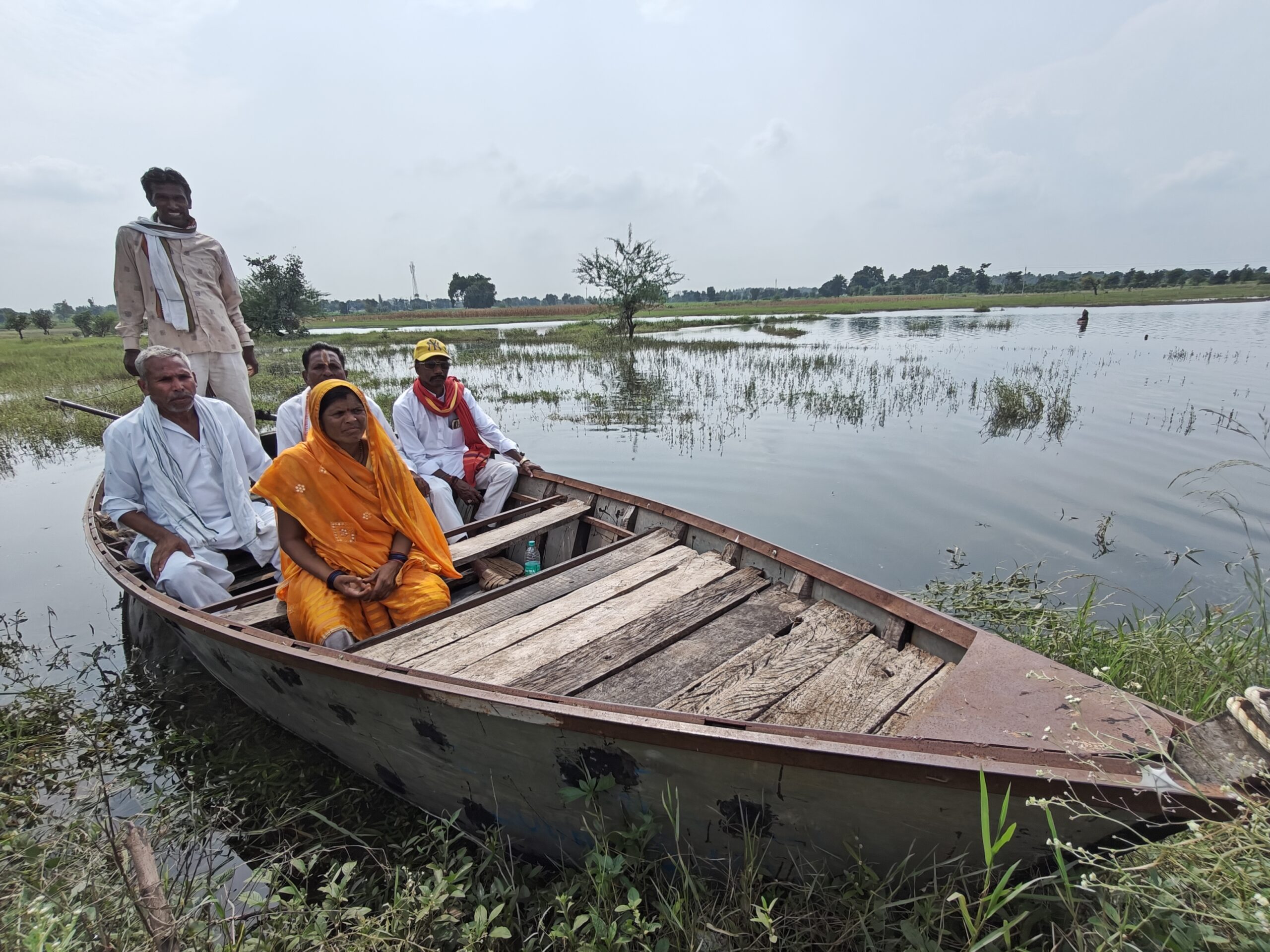 Photo showing various villagers in India sitting in a wooden boat on a lake with grasses and vegetation around them