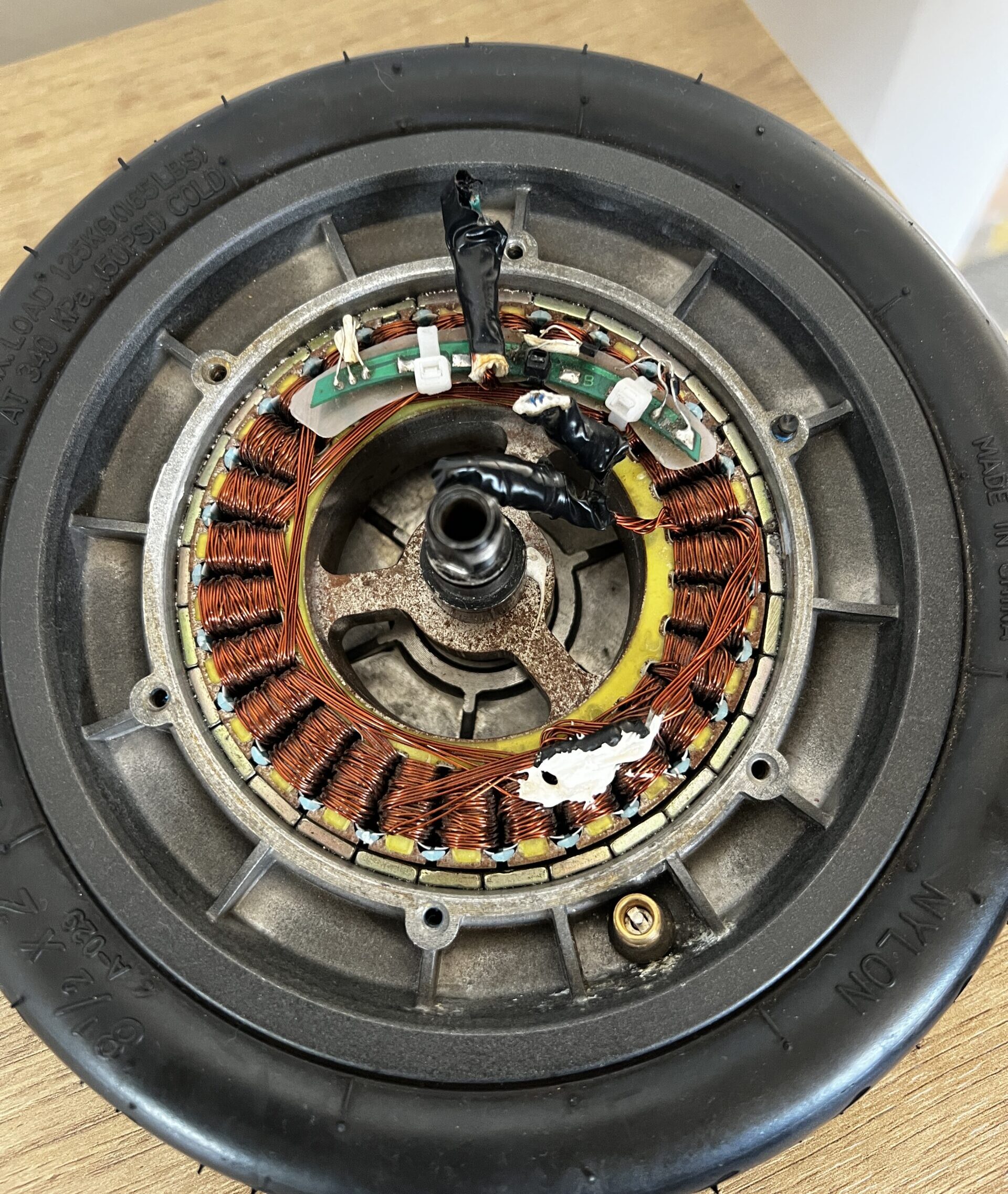 A photo of the inside of a scooter wheel, with rubber on the outside and copper wiring and other electronics on the circular inside.