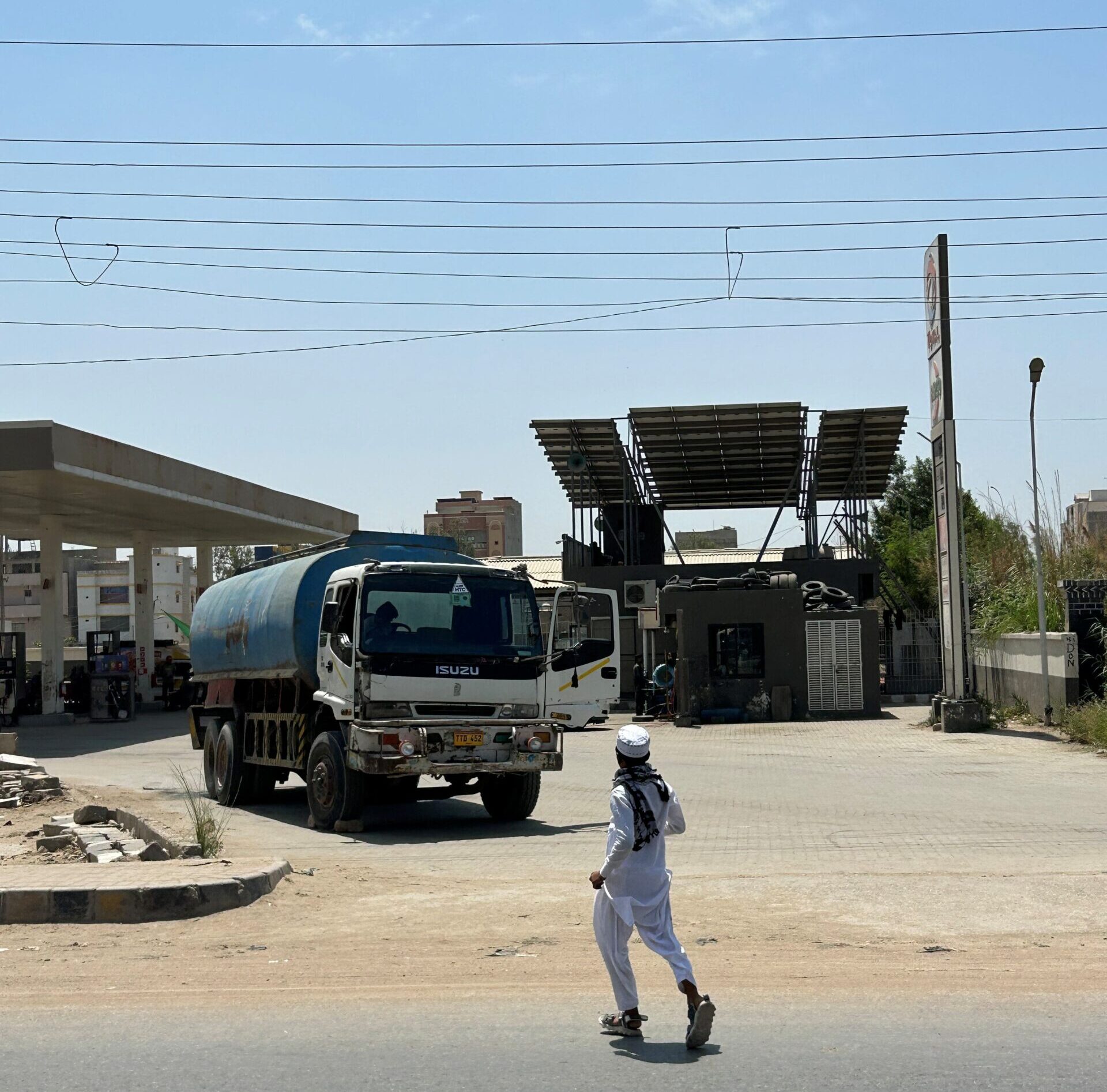 A man jaywalks across a busy highway towards a gas station that is covered with solar panels in Karachi near Port Qasim. Photo by Amena H. Saiyid