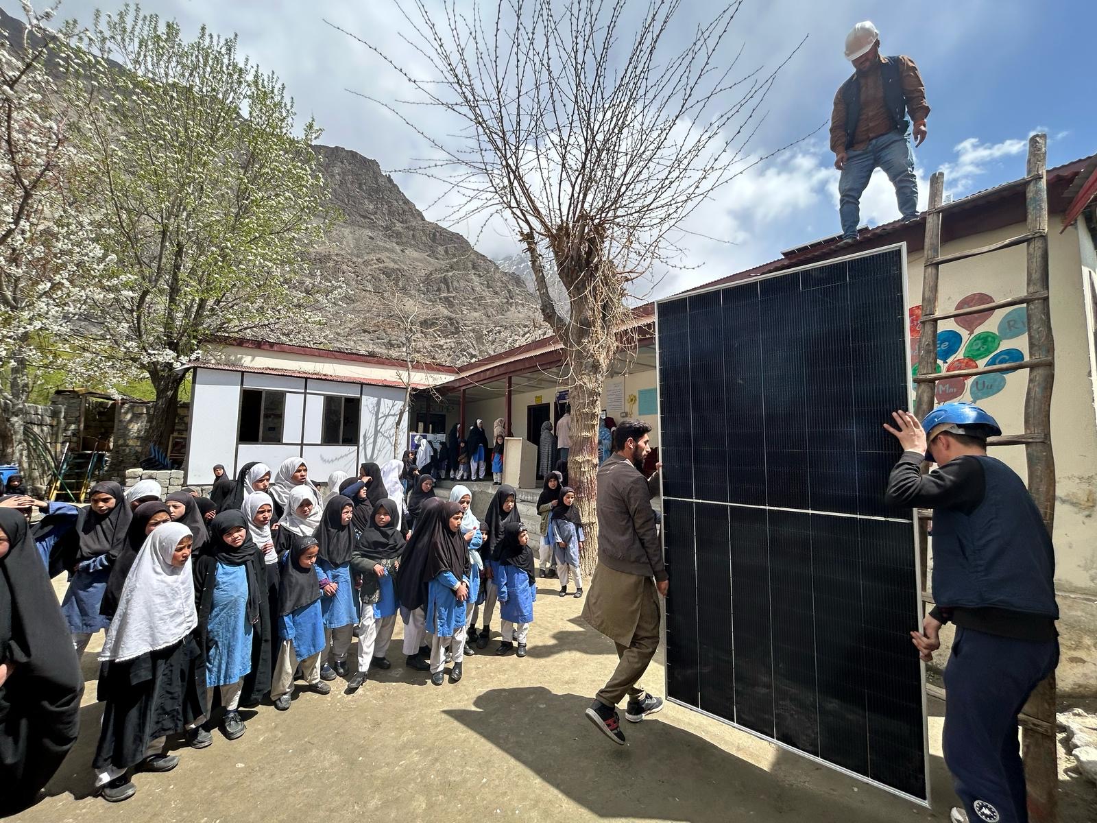 Schoolchildren shade their eyes from the strong sunlight as they watch the solar panels hoisted to the roof of their community school in Nar in Northern Pakistan. Photo by Amena H. Saiyid